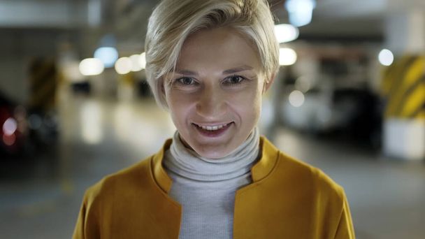 Muotokuva, Nuori liike blondi nainen hymyilee maanalaisessa autotallissa - Valokuva, kuva