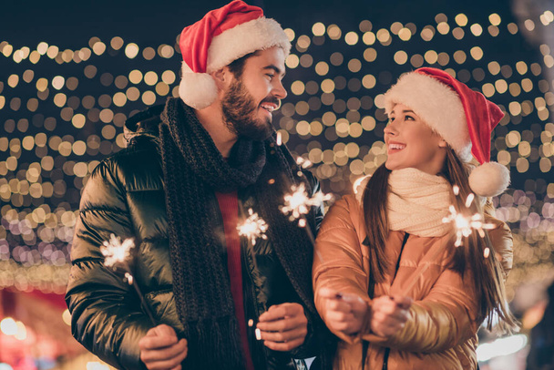 Foto di due amici che tengono le luci del bengala sotto x-mas tradizione sera all'aperto illuminazione indossare cappelli Babbo Natale - Foto, immagini