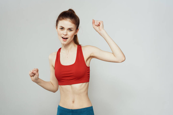 Uma mulher em uma camiseta vermelha em um fundo leve está envolvida em gestos de fitness com as mãos uma figura fina.  - Foto, Imagem
