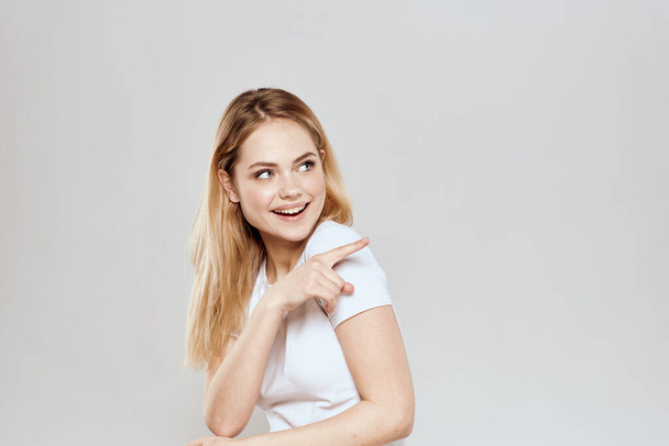 fröhliche Blondine im weißen T-Shirt gestikuliert mit ihren Händen vor hellem Hintergrund - Foto, Bild