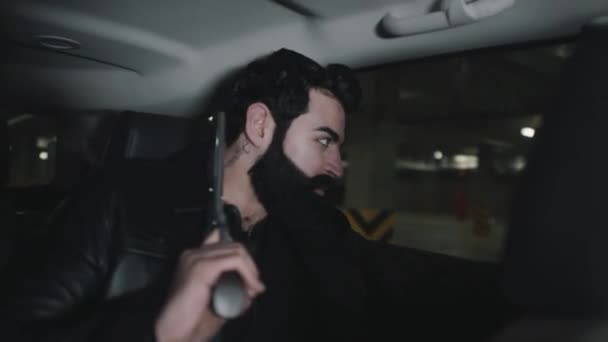 Moyen gros plan de gangster arabe barbu tenant pistolet dans les mains assis sur le siège arrière de la voiture s'échappant du parking souterrain chassant les ennemis - Séquence, vidéo