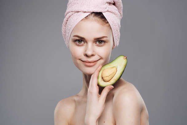 vrouw met bared schouders avocado in handen bijgesneden uitzicht over grijze achtergrond - Foto, afbeelding