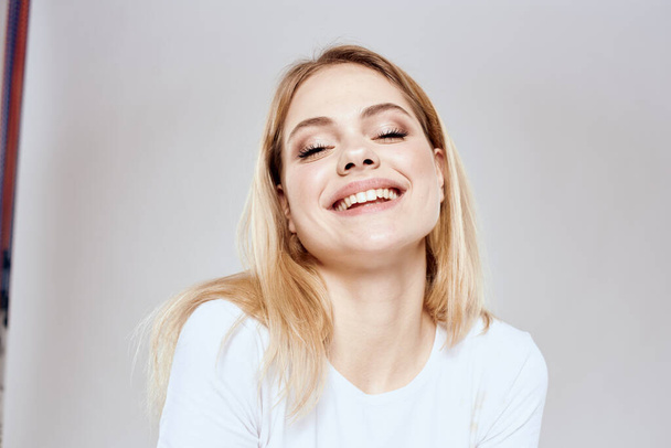 Χαρούμενη ξανθιά με λευκό μπλουζάκι που κάνει χειρονομίες με το φως των χεριών της - Φωτογραφία, εικόνα