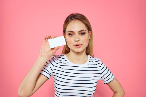 Woman with a business card in her hands a striped T-shirt pink background Copy Space advertising - Fotografie, Obrázek