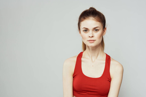Uma mulher em uma camiseta vermelha em um fundo leve está envolvida em gestos de fitness com as mãos uma dieta de figura fina. - Foto, Imagem