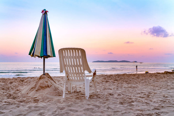Białe krzesło i parasol na tropikalnej plaży z pomarańczowym niebem  - Zdjęcie, obraz