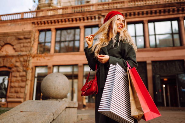 Elegant woman wearing stylish red beret with shopping bags in the city street. Autumn shopping. Consumerism, purchases, black friday, lifestyle concept. - Foto, Imagen