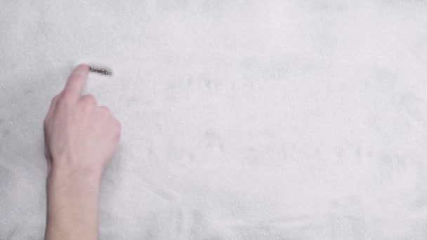Man hand schrijft het woord suiker op een achtergrond van witte suiker - Video