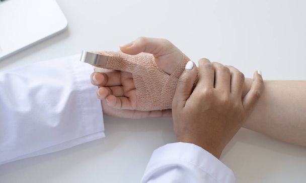 Врач смотрит на шину пальца пациента, палец прямо с ортопедическим устройством, лечение или обследование состояния пациента - Фото, изображение