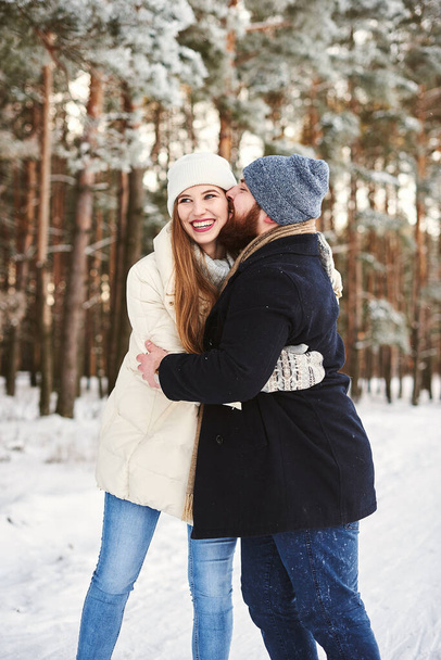 Ein junges verliebtes Paar küsst sich in einem verschneiten Winterwald. Romantische Beziehung. Liebespaar umarmt sich im Winterpark. Paar am Valentinstag im Winterpark. Mädchen in Puffjacke und Kerl im schwarzen Mantel. - Foto, Bild