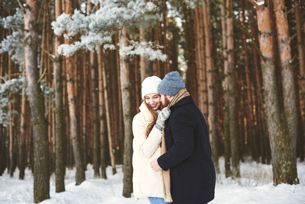 Приємна усміхнена пара обіймає одне одного у засніженому сосновому лісі на вулиці. День і зима Валентина. Безкоштовний простір, Різдвяна концепція, Xmas Morning. Разом проводимо різдвяні канікули - Фото, зображення