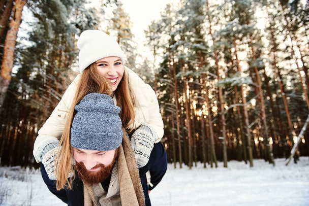 Mężczyzna daje kobiecie jazdę na barana na zimowych wakacjach w śnieżnym lesie. Tło z miejsca tekstowego dla promocji lub stronie internetowej o podróżach w sezonie zimowym. Koncepcja aktywności na wakacje zimowe - Zdjęcie, obraz