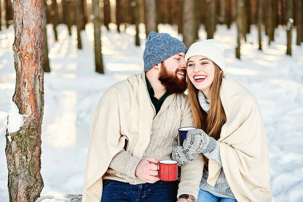 Romantyczny związek i koncepcja wakacji zimowych. Szczęśliwy uśmiechnięta para pod ciepłą kratę z filiżanek gorących napojów przytulanie i całowanie na świeżym powietrzu w zimowym lesie. Romantyczna para zakochanych - Zdjęcie, obraz