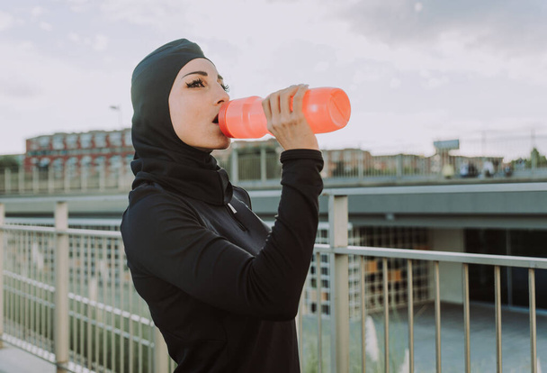Muslim sportive girl with fit body training outside - Beautiful woman with hijab doing some sport exercises, concepts about health, lifestyle and functional training - Foto, imagen