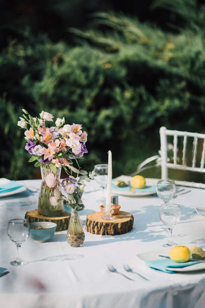 Moderne rustieke tafel voor een tuinfeest. Buiten bruiloft receptie decor, jubileum viering of elegante doop dineren. Kleurrijk en romantisch diner opgezet met bloemen en kaarsen. - Foto, afbeelding