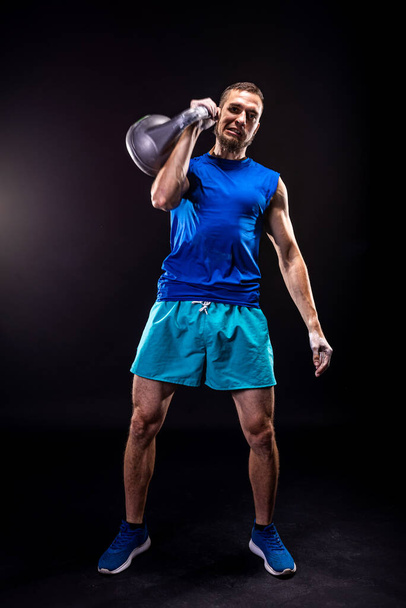 A man in a blue T-shirt and shorts trains with a kettlebell. Fitness with kettlebell. - Foto, Imagem