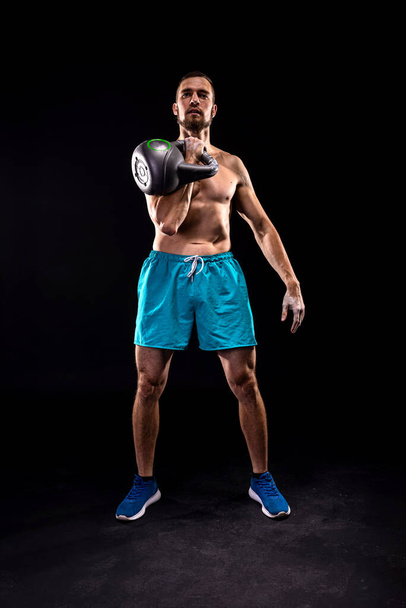 Sporty man doing weight training with kettlebell on a black background. Crossfit. Fitness with kettlebell. - 写真・画像