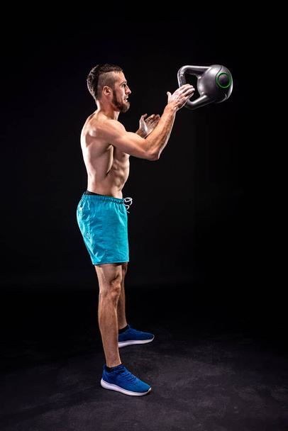 Sporty man doing weight training with kettlebell on a black background. Crossfit. Fitness with kettlebell. - Foto, immagini