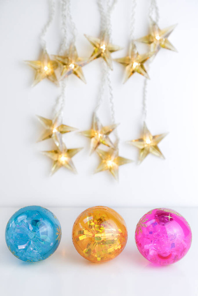 Τρεις πολύχρωμες χριστουγεννιάτικες μπάλες και μερικά φώτα σε σχήμα αστεριού σε λευκό φόντο. Αντιγραφή χώρου - Φωτογραφία, εικόνα