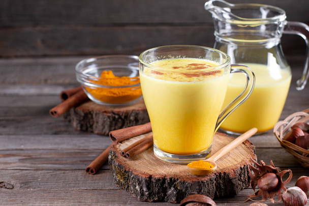 Tradiční indický nápoj kurkuma zlaté mléko ve sklenici s ingrediencemi, zázvor, kurkuma, med na rustikálním dřevěném stole. Mezera pro text - Fotografie, Obrázek