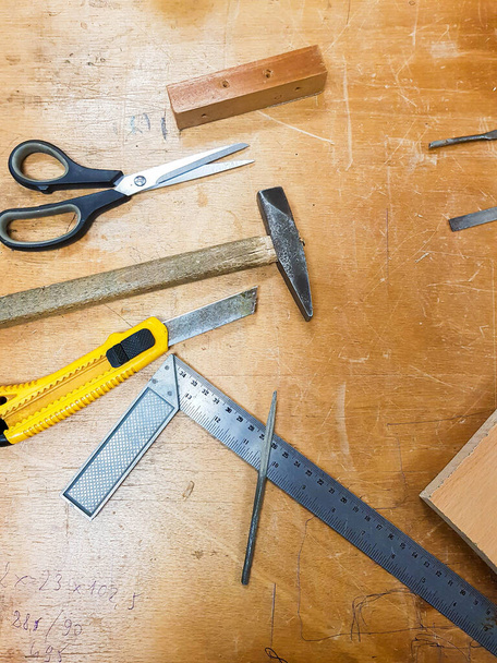 Varias herramientas de taller: cuchillo de corte de caja, tijeras, martillo y una regla de metal en una mesa de trabajo de madera tradicional. Elaboración de carpintería artesanía espacio de trabajo concepto de fondo creativo, vista superior - Foto, Imagen