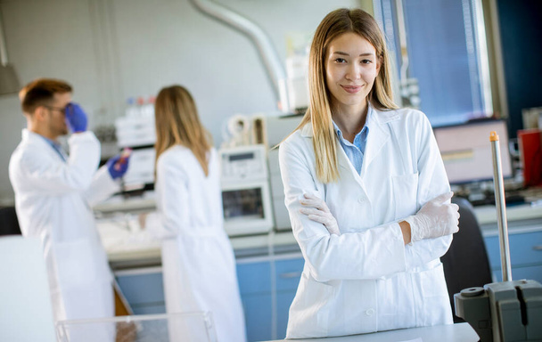 Joven científica con bata blanca de laboratorio parada en el laboratorio biomédico - Foto, imagen