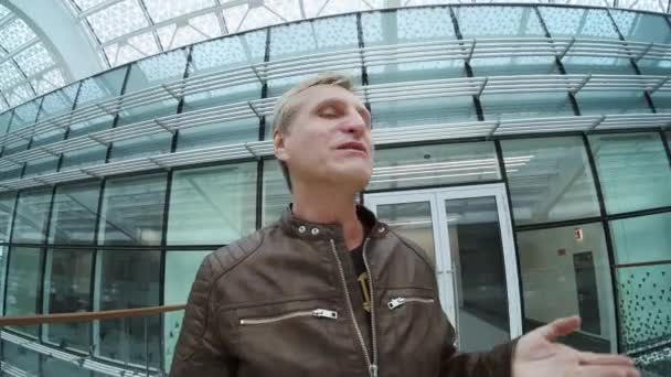 Voyageur masculin parlant à la caméra tout en marchant dans un bâtiment moderne - Séquence, vidéo