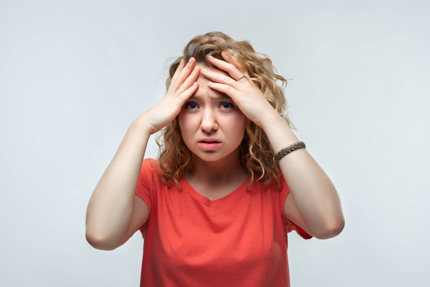 Photo of upset woman with curly hair in casual t shirt grabbing her head and rubbing temples because of headache. Studio shot, white background. Human emotions, facial expression concept - Fotoğraf, Görsel