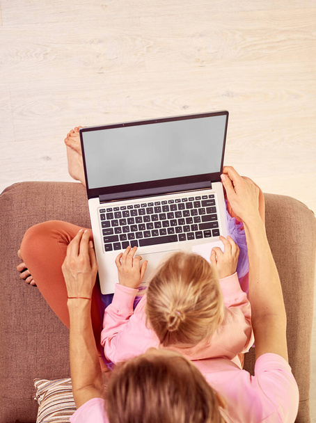 Мать и дочь используют ноутбук дома. Сидя на диване в розовой одежде вид сверху - Фото, изображение