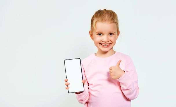 Hymyilevä pieni kaunis tyttö vaaleanpunainen osoittaa valkoinen tyhjä näyttö matkapuhelimen tekstitilaa eristetty valkoisella taustalla. Vapaa tila mainoksille. - Valokuva, kuva