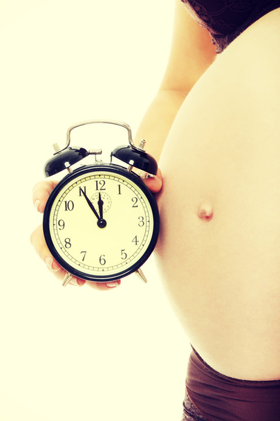 Belly of a pregnant woman with alarm clock  - Фото, изображение