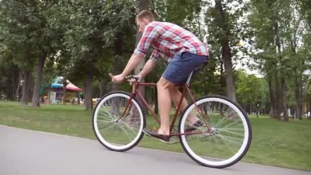 公園の道路でスポーツマンがサイクリングしている。ヴィンテージ自転車のアウトドアに乗っている若いハンサムな男。健康的な生活様式。サイドビューを閉じるスローモーション - 映像、動画