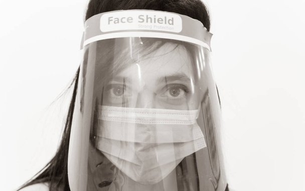 Monocromo primer plano de la cara de útero caucásico protegido por el escudo facial y máscara facial quirúrgica verde. Enfermera con equipo de protección antivirus. - Foto, Imagen