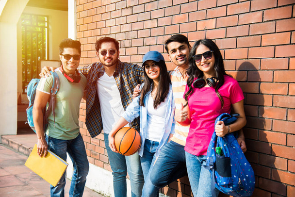 学生や友人の陽気なインドのアジアの若いグループが一緒に座って、立って、またはキャンパス内を歩いて笑って - 写真・画像