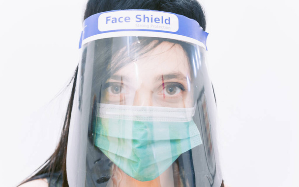Zbliżenie na białą twarz chronioną tarczą i zieloną maską chirurgiczną. Pielęgniarka w antywirusowym sprzęcie ochronnym. - Zdjęcie, obraz