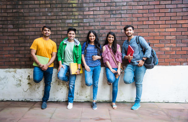 joyeux indien asiatique jeune groupe de collège étudiants ou amis rire ensemble tandis que assis, debout ou marcher dans campus - Photo, image