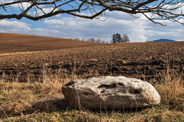 Grande pierre blanche à côté du champ labouré ondulé au début du printemps
 - Photo, image