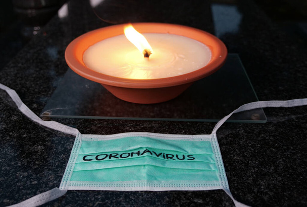 Coronavirus outbreak concept. Death caused by coronavirus, victims of Covid-19 virus. Candle light and medical mask at tombstone in the cemetery. Closed cemeteries because of Covid-19 pandemic.  - Fotoğraf, Görsel