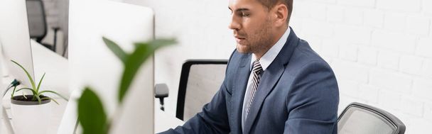 Орієнтований керівник, що сидить біля монітора комп'ютера на робочому місці на розмитому передньому плані, банер
 - Фото, зображення