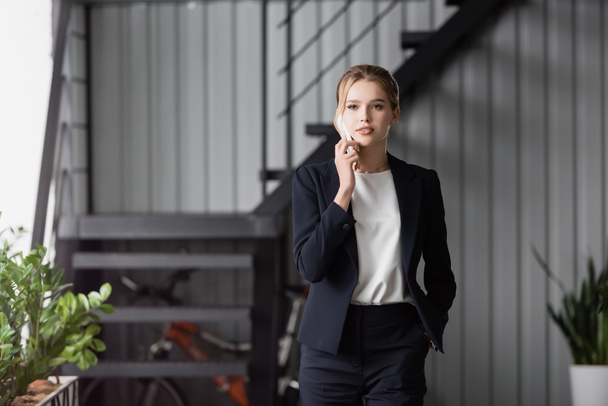 Female executive with hand in pocket looking away, while talking on mobile phone on blurred background - Fotoğraf, Görsel
