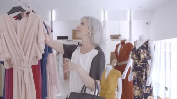Сосредоточенная продавщица, собирающая платье со стойки - Кадры, видео