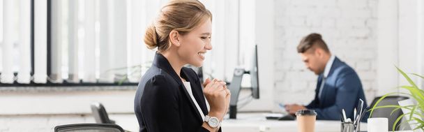 Empresária feliz olhando para laptop, enquanto sentado no local de trabalho em fundo turvo, banner - Foto, Imagem