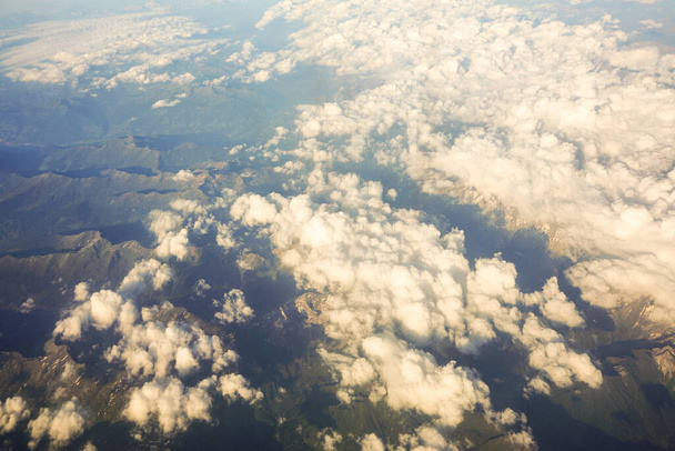 Nubes sobre montañas austríacas cubiertas de nieve vistas desde una ventana de avión, Europa - Foto, imagen