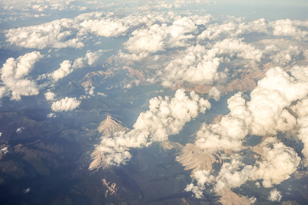 Wolken over sneeuw bedekte Oostenrijkse Alpen bergen gezien vanuit een vliegtuigvenster, Europa - Foto, afbeelding