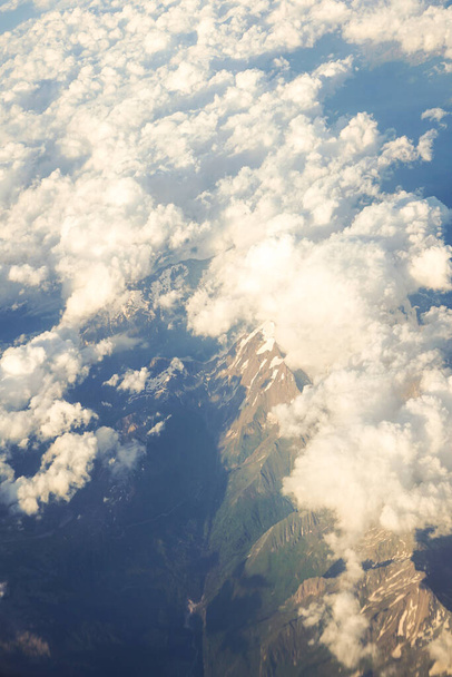 Σύννεφα πάνω από χιόνι επενδυμένα αυστριακές Άλπεις βουνά δει από ένα παράθυρο του αεροπλάνου, Ευρώπη - Φωτογραφία, εικόνα