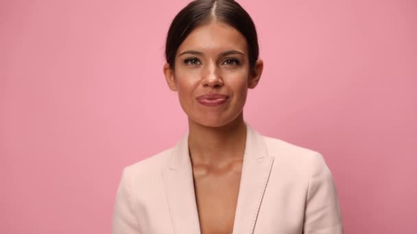 zelfverzekerde jonge vrouw in roze pak knikken, wijzende vingers en glimlachen op roze achtergrond - Video