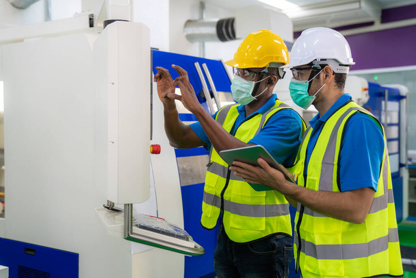 Ασιάτες βιομηχανικοί μηχανικοί και εργαζόμενοι σε σκληρά καπέλα συζητούν τη γραμμή προϊόντων ενώ χρησιμοποιούν την ψηφιακή ταμπλέτα στη μηχανή κοπής άλεσης cnc σε ένα εργοστάσιο κατασκευής βαρέων βιομηχανιών. - Φωτογραφία, εικόνα