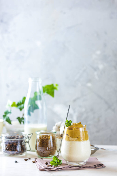 Glass of Iced Dalgona Coffee, a trendy fluffy creamy whipped coffee, decorated by mint. White wooden table surface. - 写真・画像