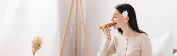 joven morena mujer con vitiligo comer croissant, bandera - Foto, Imagen