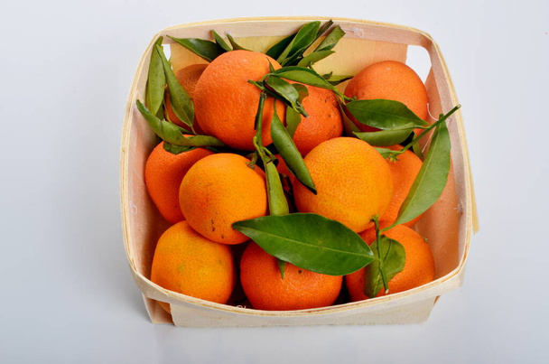 Szerves mandarin zöld levelekkel, fa kosárban, fehér alapon - Fotó, kép